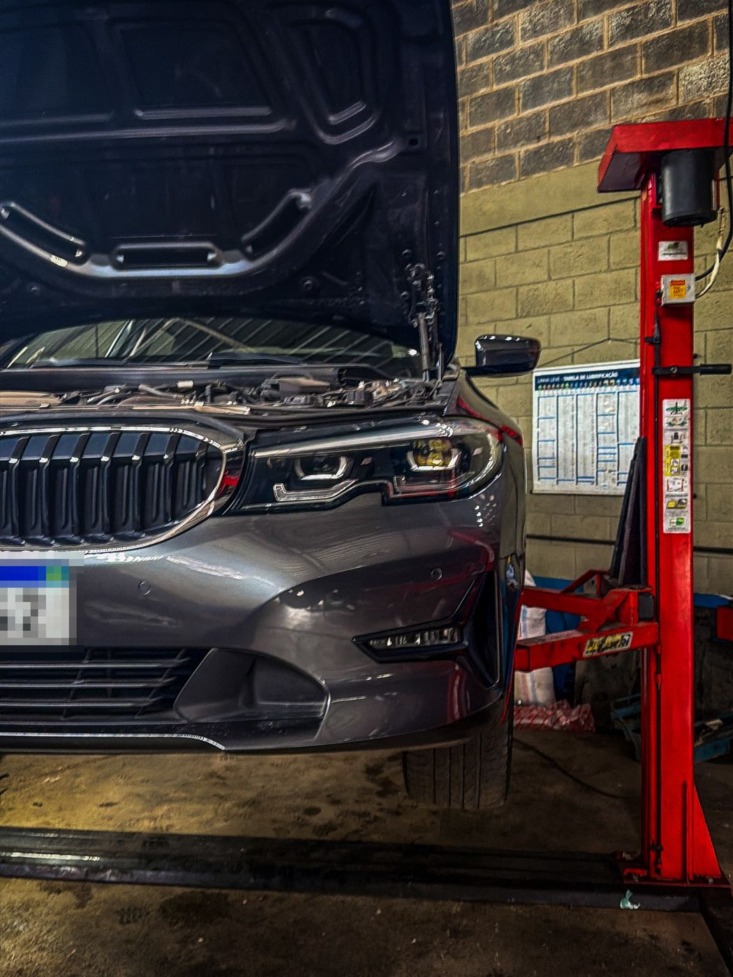 BMW Série 3 com o capô aberto ao lado de um elevador vermelho na oficina