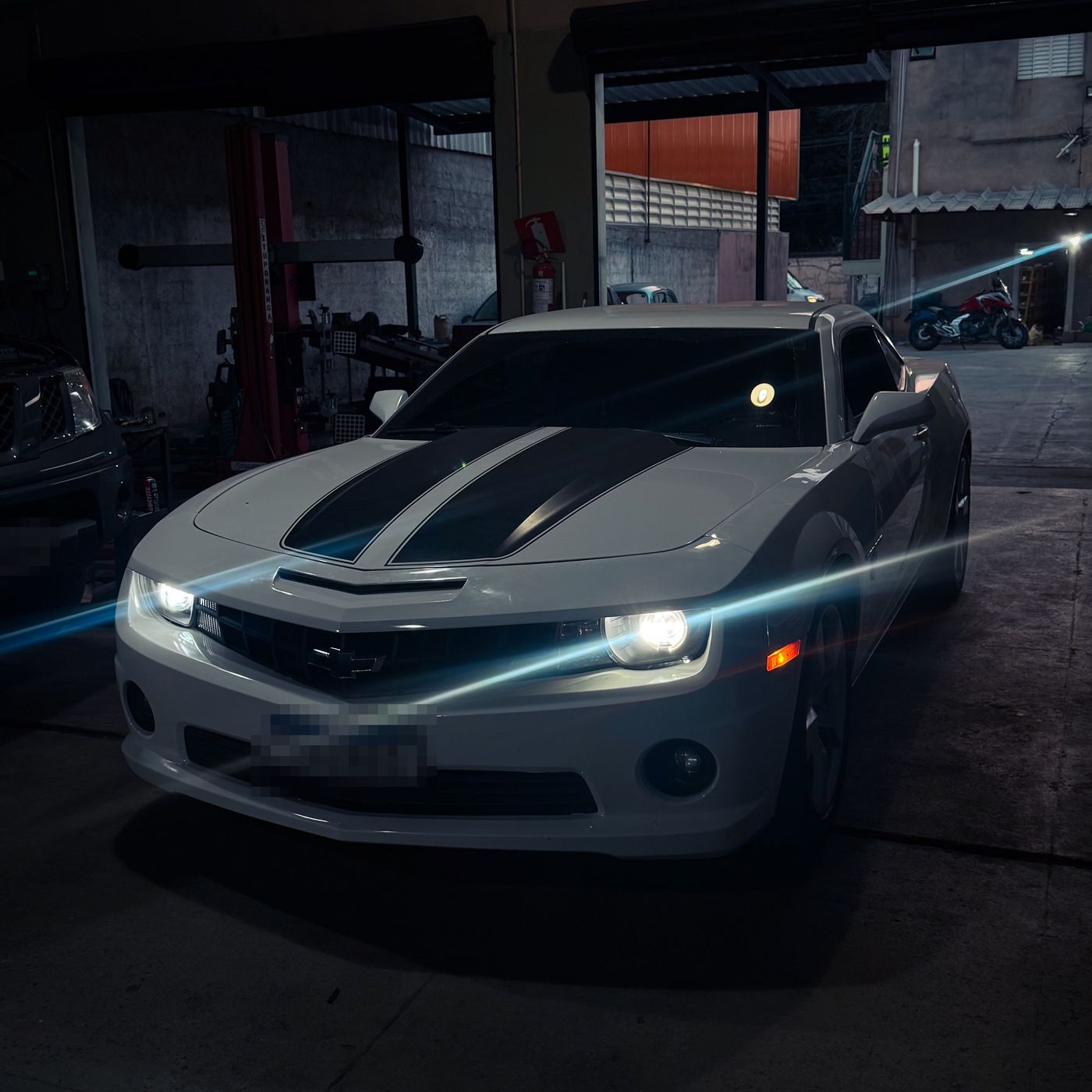 Chevrolet Camaro branco com faróis acesos na oficina à noite
