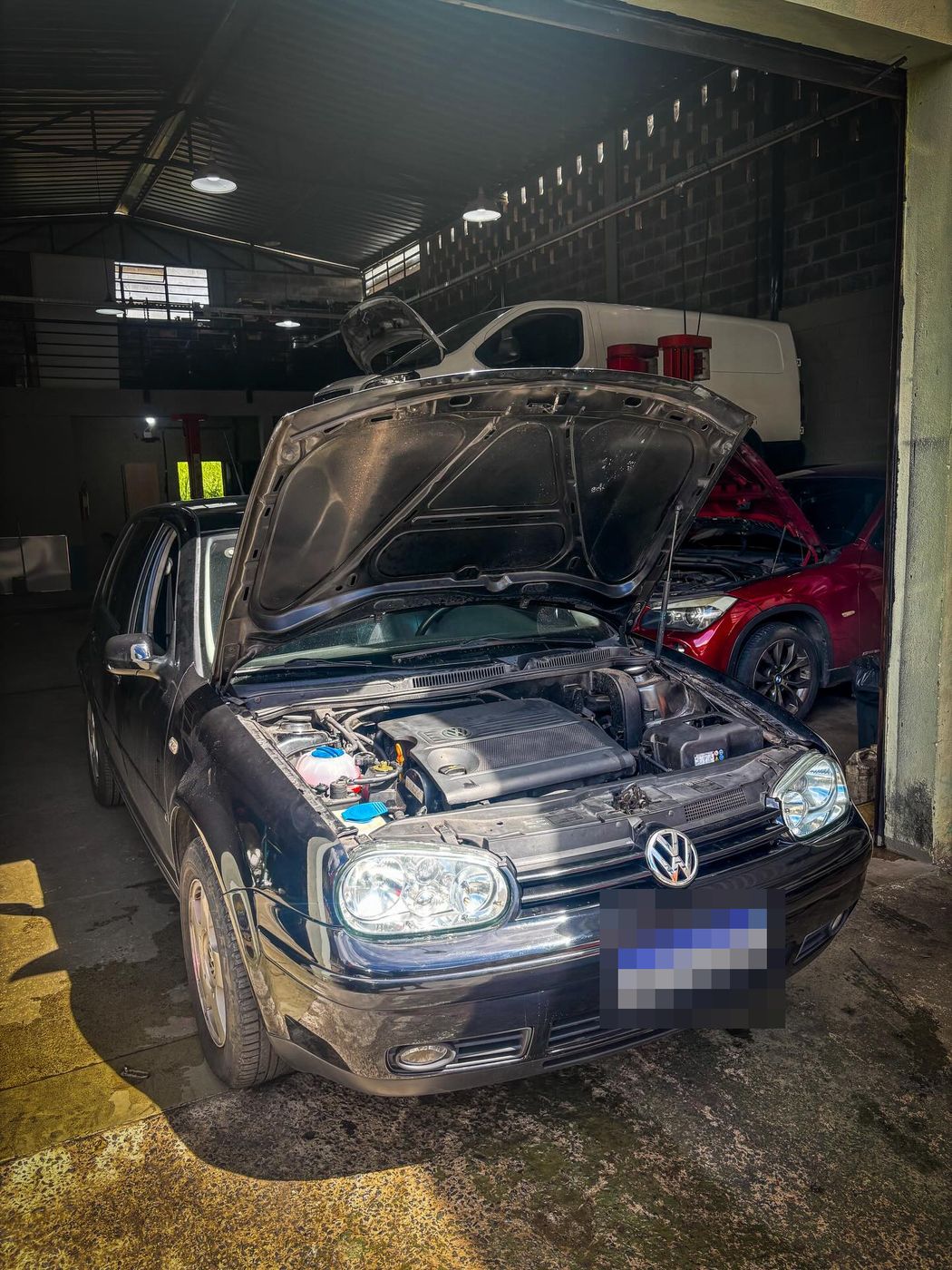 VW Golf preto com o capô aberto na entrada da oficina